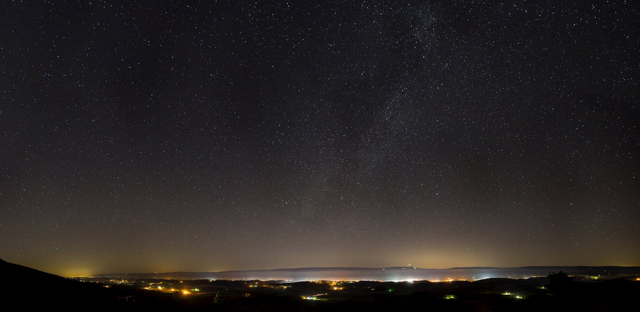 A breathtaking view of a starry night sky over an illuminated urban landscape, perfect for astronomy enthusiasts.