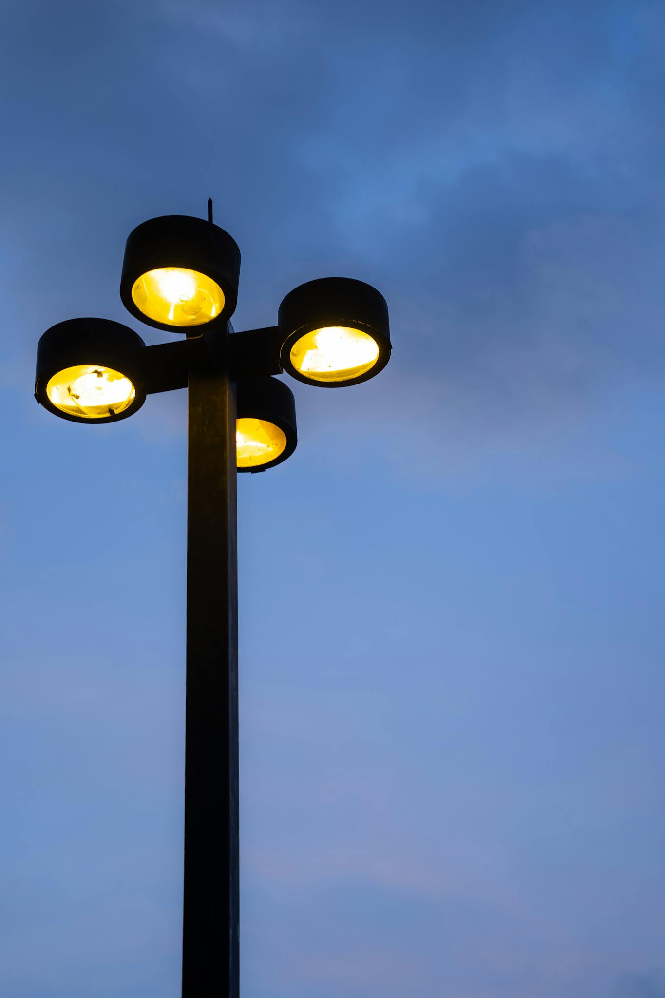 A close-up view of a four-armed streetlamp glowing against a twilight sky.